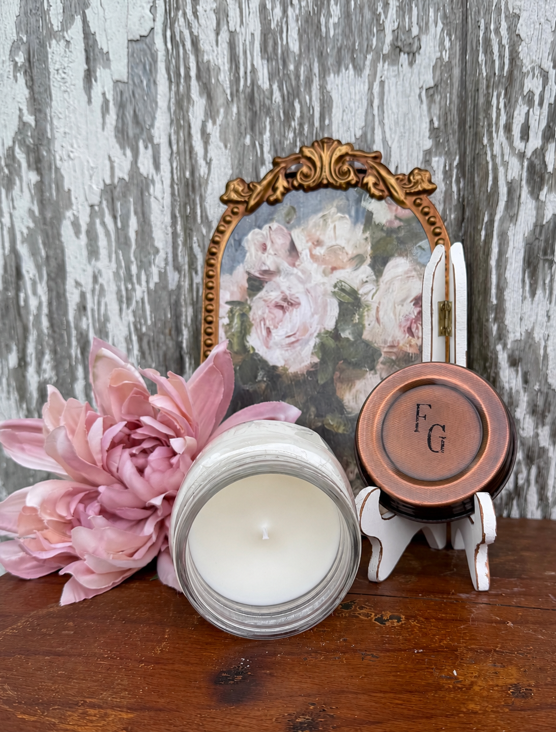Decorative setup with a candle, pink flowers, and a small framed picture on a wooden surface.