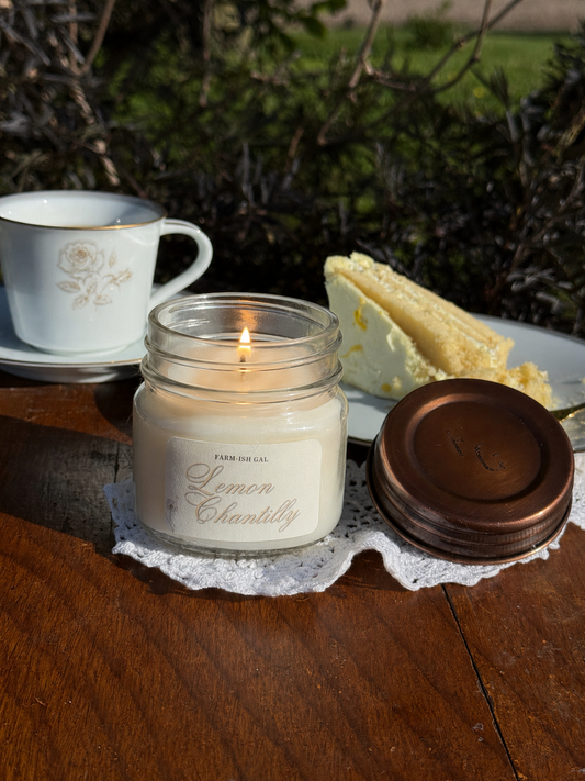 lit candle with a label that says Lemon Chantilly, with a cup of coffee and a piece of cake next to it.