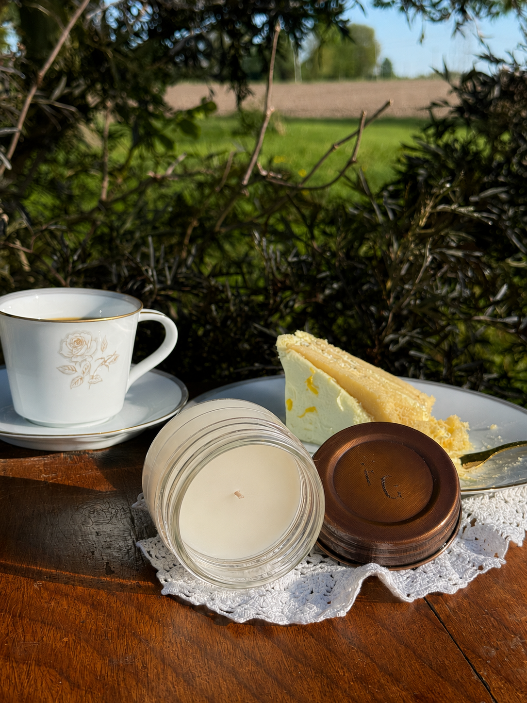  Candle laying on its side with the lid off on a wooden table with a cup of coffee and a piece of cake.
