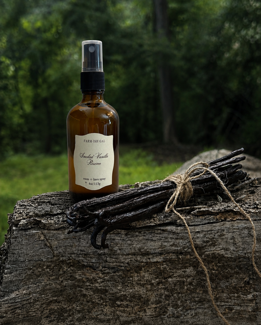 Fine mist spray bottle with a label that says Smoked Vanilla Reserve with vanilla beans on a wooden log outdoors